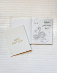 Two greeting cards on a textured white surface, one with a swan illustration and text, the other with 'baby's first year' text.