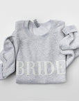 Folded army gray crewneck sweatshirt with large white-embroidered “BRIDE” lettering across the chest on a plain white background.