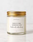 A 4 oz glass jar candle with a gold metal lid and a white label that reads 'feelsblossom' and 'SMELLS LIKE MIMOSAS AND lastminute adventures' on a light marble surface.