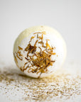 Chamomile bath bomb in its round shape with chamomile pieces around it on a white background.
