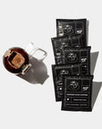 Copper Cow Vietnamese Coffee, mug with a metallic pour-over filter on the left and four packets of the Vietnamese coffee in its black sachets with white lettering, all arranged on a clean white surface.