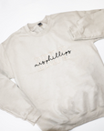 Custom embroidered cream-colored crewneck sweatshirt. Embroidered on the front are the words "BRIDE" in a block-letter font in ivory thread and the words "mrs Phillips" in a more delicate cursive style in black thread on a white background.