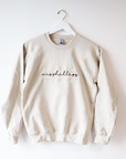 A cream-colored crewneck sweatshirt. Embroidered on the front are the words "BRIDE" in a block-letter font in ivory thread and the words "mrs Phillips" in a more delicate cursive style in black thread on a white background, hung on a white wooden hanger.
