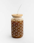 A smiley print glass cup image is shown, in its glass cup with a printed white smiley with a wooden lid and a glass straw with coffee inside on awhite background.