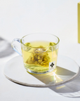 Clear glass mug with green tea and a tea bag on a white surface