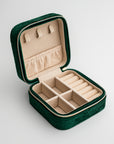 Emerald velvet jewelry box, close-up photograph showcases an emerald velvet jewelry box, opened to display its beige interior compartments and organizers, set against a clean white backdrop.