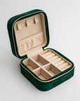 Emerald velvet jewelry box, close-up photograph showcases an emerald velvet jewelry box, opened to display its beige interior compartments and organizers, set against a clean white backdrop.