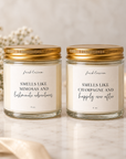 Two 4 oz glass jar candles with gold lids and cream labels, displayed on a marble surface with soft decorative flowers and ribbon. The labels read 'fresh lemon' and 'SMELLS LIKE MIMOSAS AND lastminute adventures' on the left, and 'SMELLS LIKE CHAMPAGNE and happily ever after' on the right.