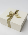 A cream-colored rectangular gift box tied with a satin gold ribbon and bow, photographed on a clean white background.