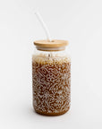Image of glass straw tumbler with a floral design with the bamboo lid filled with iced coffee drink on a white background.