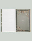 Grandma's Story memory keepsake and journal book. An open, lined journal, featuring a muted, greyish-green background framed by delicate, brown-toned leaf illustrations.