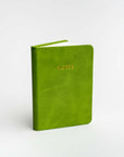 Green pocket softcover notebook featured on a white background. With Notes in gold in front of it.