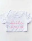 Hello, I'm new here. This onesie features pink vinyl lettering in a white onesie on a white background.