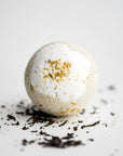 Jasmine bath bomb featured in its round shape and details, surrounded by jasmine pieces on a white background.