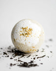 Jasmine bath bomb featured in its round shape and details, surrounded by jasmine pieces on a white background.
