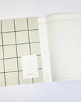 over featured, a rectangular planner, its surface marked by a dark gray grid over a pale beige background. Positioned on the lower right, a white rectangular label provides details of the planner in black lettering.
Showing one of the pages inside of the planner.