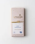 Moonstruck creamy chocolate bar in its rectangular-shaped package that is pink with gold spots, gold lettering, and a white label with blue letters and two symbols in blue wrapped in a gold bow on a white background.