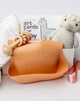 New baby girl gift box, A front view of a Baby Girl Gift Box featuring a knitted cute elephant holding roses, a floral swaddle, a wooden rattle, the book Guess How Much I Love You, and a pink silicone bib with an engraved name, all arranged in a white gift box with ivory shred and tied with a pink ribbon on a white background.