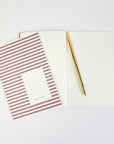 Image of opened and closed bordeaux stripped notebook with gold pen.