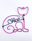 Personalized cat ornament, image shows the cat ornament done in pink wire that forms the outline of a cat's body and head with a white bow and a silver bell. In the center is personalized with the name Chloe in black aluminum wire.
