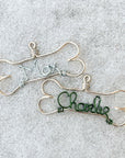 Personalized dog ornament image that shows two of them in bone-shaped outline gold aluminum wire with the names Max in silver color and Charlie in green aluminum wire in a grey background.