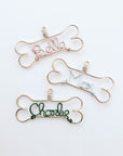 Personalized dog ornaments image that shows three of them in gold aluminum wire dog bone shaped outline, with the names Bella in rose gold, Max in ice blue and charlie in green color aluminum wire.