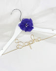 white hanger with silver hook, personalized with gold aluminum wire with the name "Sophia" and a dark purple chiffon flower. on a white background and chiffon white fabric.