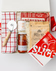 A white gift box with ivory paper shred and tied with a red ribbon on a white background. Inside the box are a Slice: Pizza Recipes book, a circular pizza cutter, a red grid tea towel, pizza herbs in a ceramic crock, an organic pizza flour mixture, an organic all-natural pizza sauce, and artisan all-natural uncured pepperoni — a “Pizza Night” gift box.