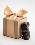 Dark chocolate sea salt caramels are featured in the front, with four pieces displayed, and behind them, the light brown cardstock gift box they come in, wrapped with an oatmeal-colored ribbon.