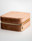 Showcases velvet jewelry box in taupe color showing its square shape and closed showing its gold zipper.