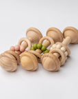 Eco-friendly wooden baby rattle with a smooth maple wood handle and simple natural design for infant play, three shown, each with a different color of silicone beads: pink, green, and beige.