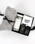 Gray 'foxblossom' socks with a black ribbon, 'herbivore' detox soaking salts in a glass jar, two 'breathe deeply' wipes in a white package, and black eucalyptus essential oil box and bottle, placed in a small black 'foxblossom' box with a black ribbon