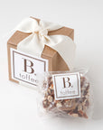 B. toffee, tucked in a cushion of chocolate crinkle paper, wrapped in a kraft box with a ivory grosgrain ribbon. Toffee in clear plastic packaging.
