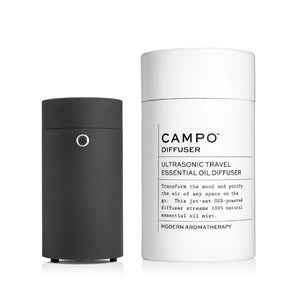 Black Campo diffuser shown next to white container tube which read "Campo diffuser, ultrasonic travel essential oil diffuser. Transform teh mood and purify the air of any space on the go. This jet-set USB-powered diffuser streams 100% natural essential oil mist. Modern aromatherapy. "