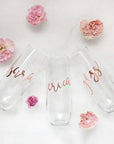 Three champagne flutes personalized in rose gold lettering with the names Sara, Erica, and Jess in a white background with five pink roses around them.