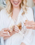 Image of a bride and two bridesmaids holding their champagne flutes personalized in gold lettering.
