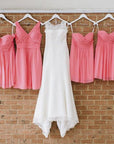 Wedding dress and bridesmaid dresses hung on custom white hangers with base wires shaped into names, holding one bridal dress and 6 pink bridesmaids' dresses.