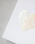 A simple yet elegant card, featuring a heart-shaped floral design rendered in gold foil, centered on a crisp white background.