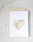 A simple yet elegant card, featuring a heart-shaped floral design rendered in gold foil, centered on a crisp white background.