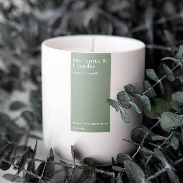 Eucalyptus & lavender candle in matte white jar with sage green label on a bed of eucalyptus.