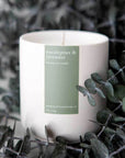 Eucalyptus & lavender candle in matte white jar with sage green label on a bed of eucalyptus.