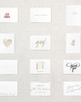 Display of twelve white cards. Gold floral heart, pink xoxo, gray branch, white congrats embossed, happy birthday under five candles, thank you in gray script, thinking of you, I couldn't tie the knot without you in gold, Yay! in gold script, will you be my bridesmaid rose gold, will you be my maid of honor rose gold, will you be my matron of honor rose gold