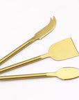 Matte gold cheese knives, set of three, gold-plated stainless steel, one pronged knife for hard cheeses, one wedge knife for semi-hard cheeses, and one tear-shaped knife for soft cheeses. Shown in a white background.