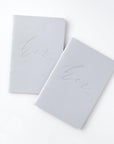 Her and her gray linen letterpressed vow books, featured in a white background