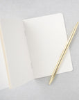 Vow book opened showing its white pages and a gold pen on top of it in a gray background.