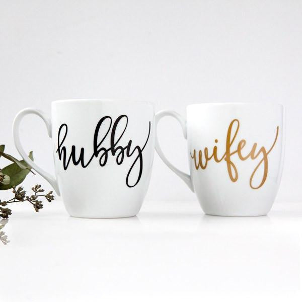 White ceramic mugs, two 15 oz mugs, "hubby" in black script font, "wifey" in gold script font