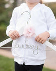 Junior Bridesmaid hoodie, a little girl in a white hoodie holds a personalized white hanger that says 'Audrey' in silver aluminum wire with a flower detail on a natural background.