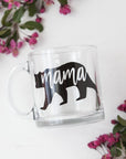 Mama bear mug featured: a transparent mug with a silhouette of a bear in black, cut out to reveal the mama bear in a white background with plants surrounding it.