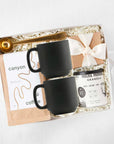 Gold clip coffee spoon, 'b toffee' with an ivory ribbon, Mocha morning granola in a cylinder can, 'canyon' coffee in a brown paper bag, and two black ceramic mugs, in ivory paper shread, in a gray 'foxblossm' box,