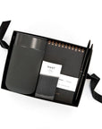 16oz dark grey Porter mug, a mini dark Mast chocolate bar, a spiral bound dark grey Appointed Pocket Notepad, and two black pens arranged inside of a small black gifting box with black shred.